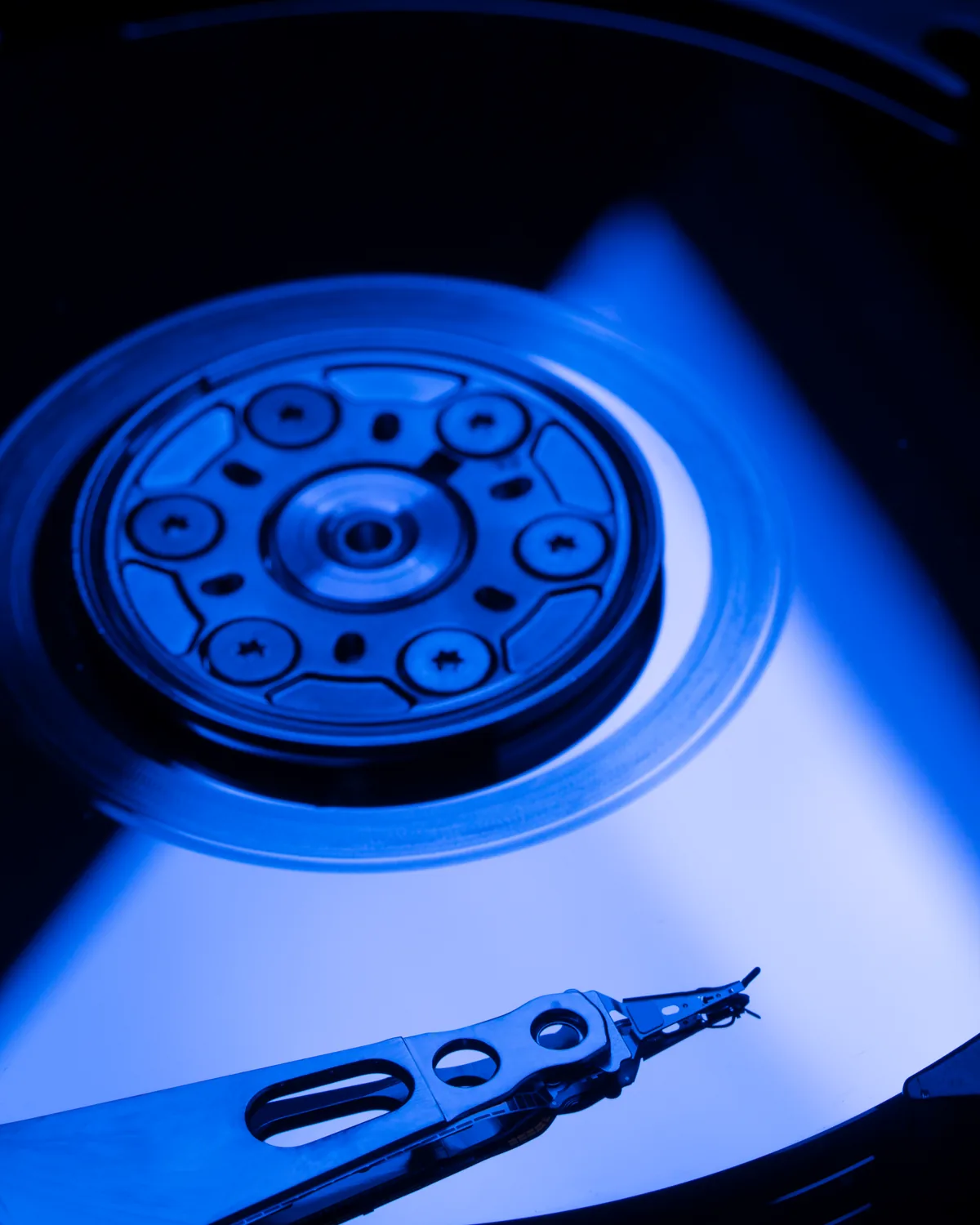 Plateau et bras de lecture d'un disque dur en gros plan, eclaires en bleu